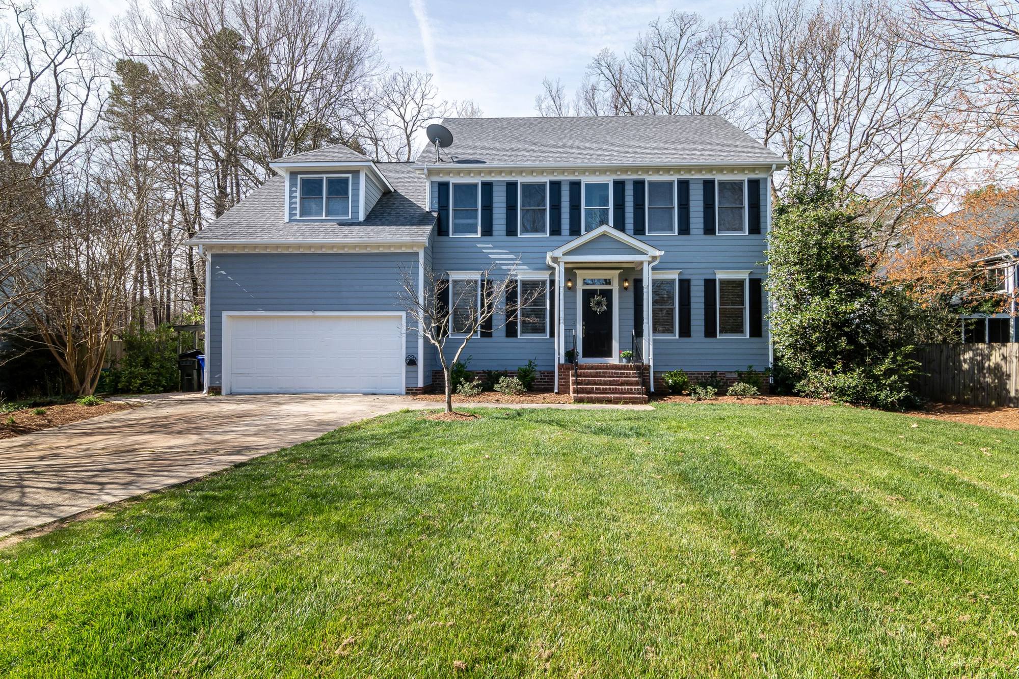 Blue two-storey colonial house with black shutters behind a freshly mowed lawn