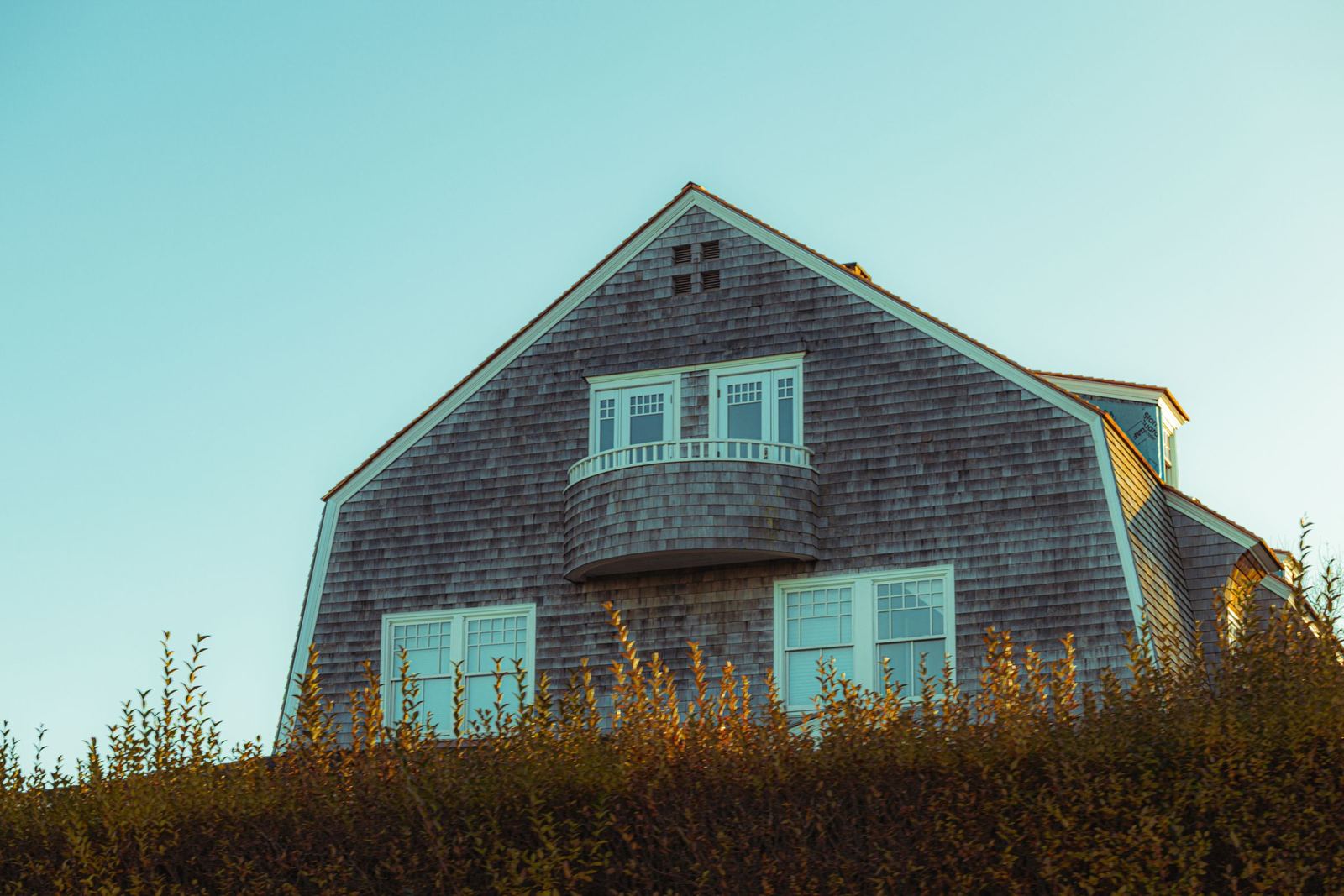 Weathered cedar-shingle house with a gambrel roof against a clear sky